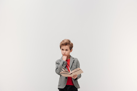 thoughtful little schoolboy with book isolated on greyの写真素材