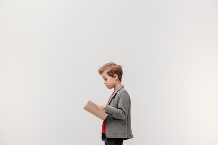 side view of stylish little schoolboy reading book isolated on greyの写真素材