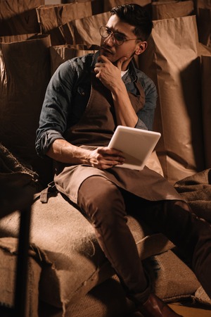 pensive young worker with tablet sitting on sack bag