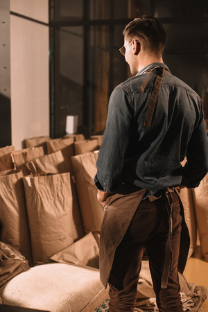 back view of coffee shop worker in apron looking at paper bags with coffee beansの写真素材