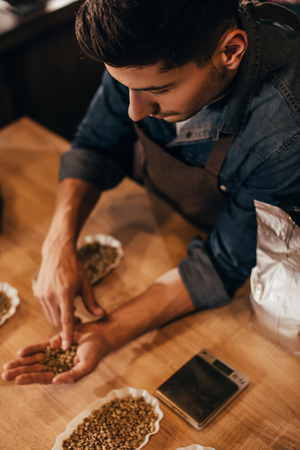 selective focus of man checking coffee beans quality at wooden tableの写真素材