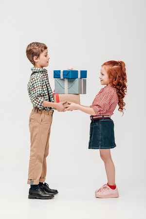 side view of adorable happy kids holding presents isolated on greyの写真素材