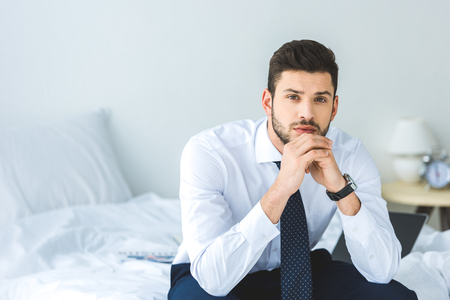 handsome businessman in white shirt and tie sitting on bedの写真素材
