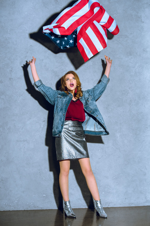 excited woman throwing american flag against concrete wallの写真素材