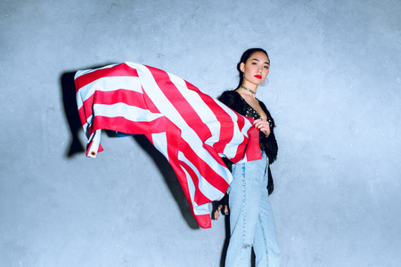 portrait of beautiful asian woman with american flag against concrete wallの写真素材