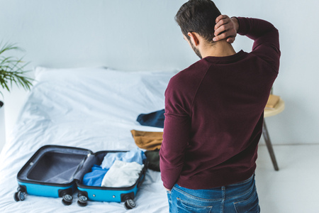 back view of thoughtful man packing baggage on bed for travelの写真素材