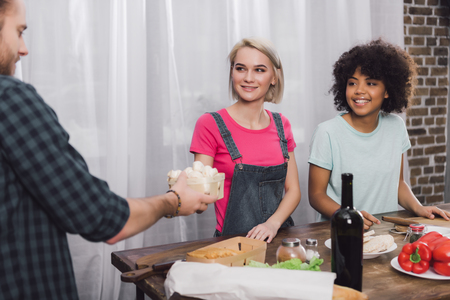 man giving mushrooms to multiethnic friends who cooking in kitchenの写真素材