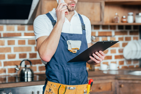 cropped shot of foreman holding clipboard and talking by smartphoneの写真素材