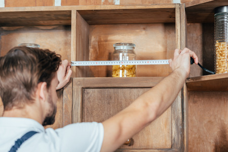 selective focus of young handyman measuring kitchen furniture with tapeの写真素材