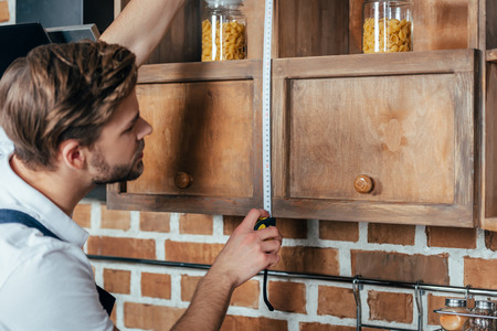 side view of young handyman measuring kitchen furniture with tapeの写真素材