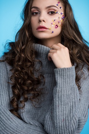 stylish long haired young woman with flowers on face in sweaterの写真素材
