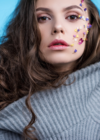 close-up portrait of woman in warm grey sweater with flowers attached to faceの写真素材
