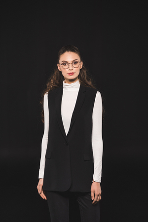 portrait of elegant stylish woman in eyeglasses looking at camera isolated on blackの写真素材