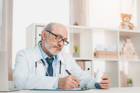 portrait of focused senior doctor making notes on notepad at workplace in clinicの写真素材