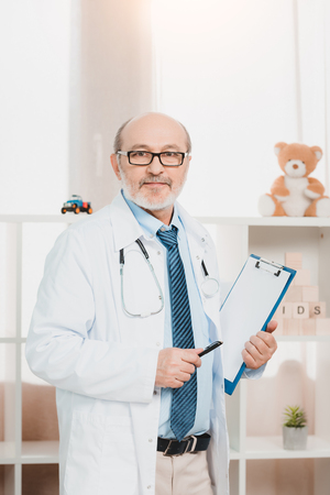 portrait of senior doctor in eyeglasses with stethoscope and notepad looking at cameraの写真素材