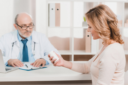 selective focus of smiling woman looking at pills in hand in clinicの写真素材