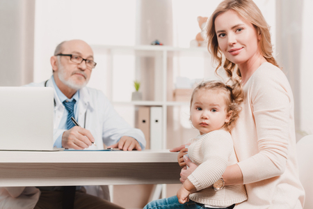 mother and little daughter looking at camera during doctors reception in clinicの写真素材