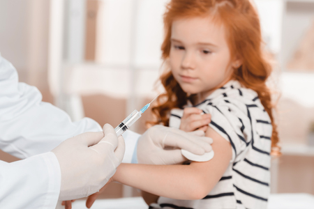 selective focus of doctor in medical gloves making injection to little girl in clinicの写真素材