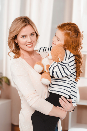portrait of smiling mother holding little daughter with teddy bearの写真素材