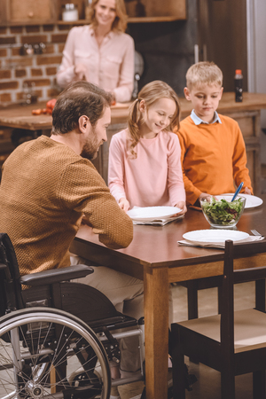 happy kids with father in wheelchair serving table for dinner at homeの写真素材