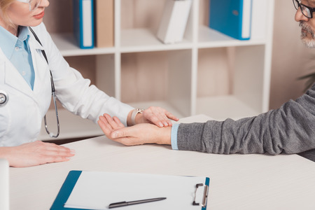partial view of female doctor checking patients pulse in clinic