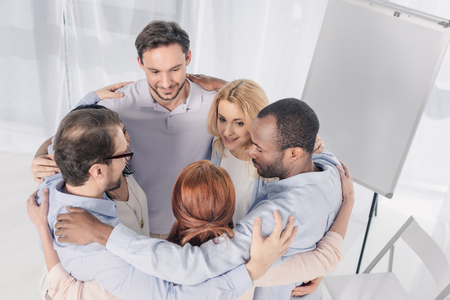 mature multiethnic people standing in circle and embracing during group therapyの写真素材