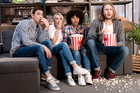 Shocked multiethnic friends watching horror movie with popcornの写真素材