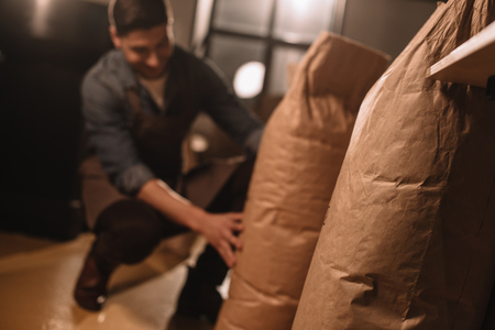 partial view of worker in apron with paper bags of coffee beans