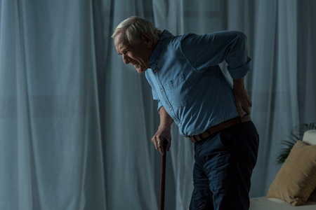 Senior man suffering from back pain leans on a caneの写真素材