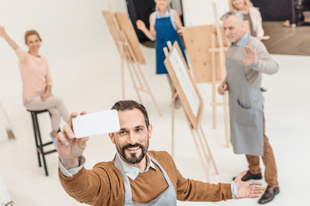 mature man with smartphone taking selfie with adult students at art classの写真素材