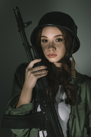 beautiful young woman in military helmet with rifle, on grey with shadowsの写真素材