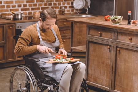 high angle view of disabled man in wheelchair cutting vegetables at homeの写真素材