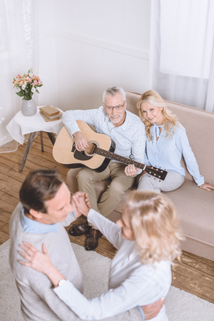 Senior men and women listening to guitar music and dancing in living roomの写真素材