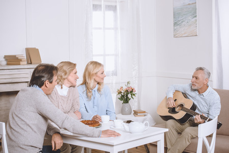 eleder man playing guitar while another people sitting at tableの写真素材