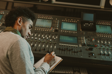 handsome young musician writing in notebook at recording studio