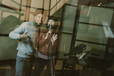 young singers couple recording song behind glass at studioの写真素材
