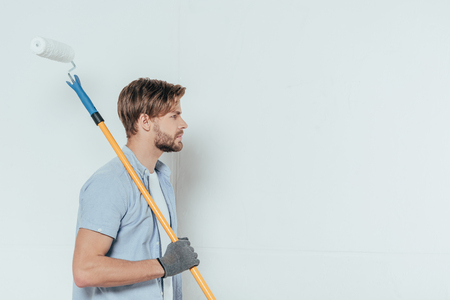 side view of young man holding paint roller and looking away on greyの写真素材