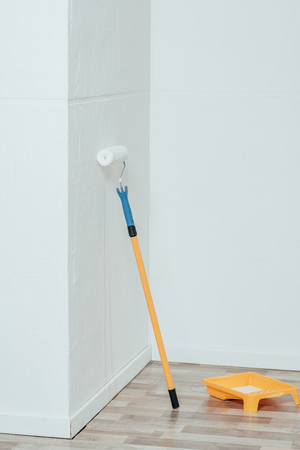 painting roller and container with white paint in empty roomの写真素材