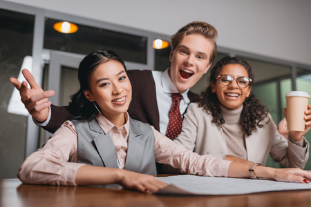 excited multicultural businesspeople with coffee and documents working in officeの写真素材