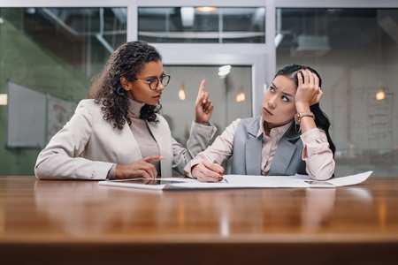 tired and serious multiethnic businesswomen working with documents in officeの写真素材