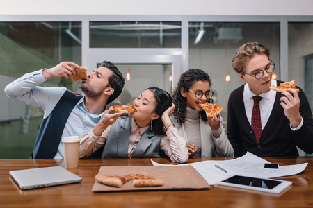 cheerful multiethnic businesspeople eating pizza in officeの写真素材