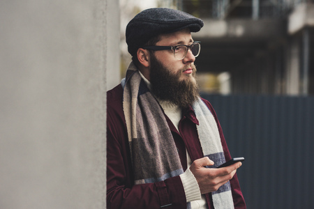 stylish thoughtful man using smartphone and leaning on wallの写真素材