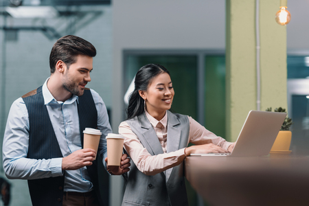 multiethnic businesspeople working with laptop and drinking coffee in officeの写真素材
