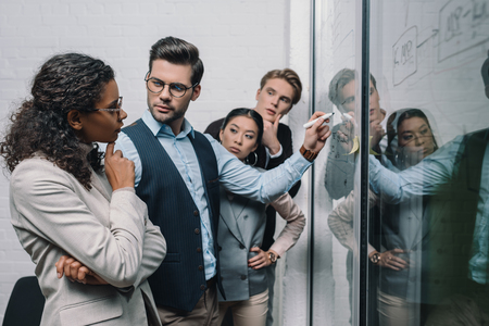 multiethnic businesspeople writing on glass board and working in officeの写真素材