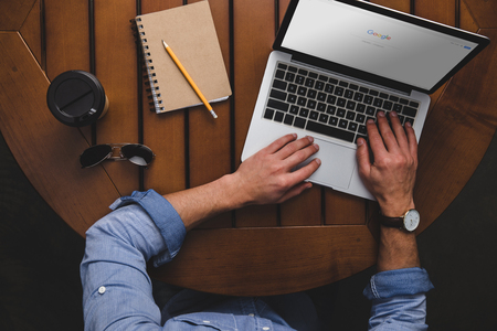 overhead view of man using laptop with google website while sitting at table with coffee and notepadのeditorial素材