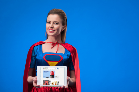 portrait of smiling woman in superhero costume showing tablet isolated on blueのeditorial素材