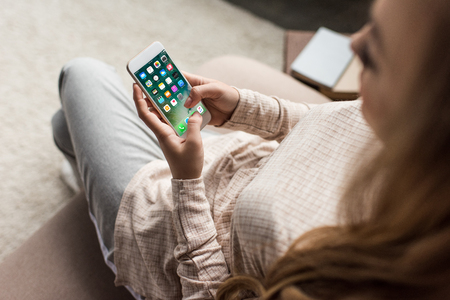 cropped shot of woman on couch using smartphone with ios apps on screenのeditorial素材