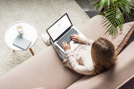 high angle view of woman at home sitting on couch and using laptop with google search on screenのeditorial素材