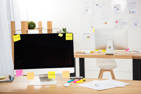 close up view of workplace with blank computer screen, sticky notes and papers in officeの写真素材