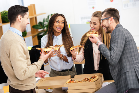 portrait of multiethnic business people eating pizza together in officeの写真素材